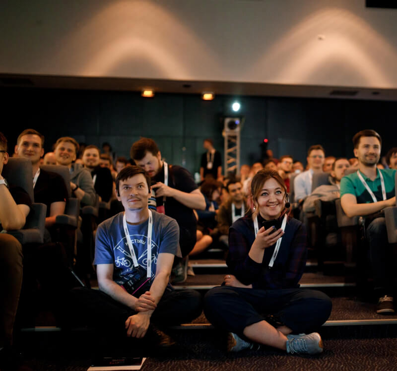 A guy and a girl watching a conference sitting on the floor in the aisle between the rows of the auditorium